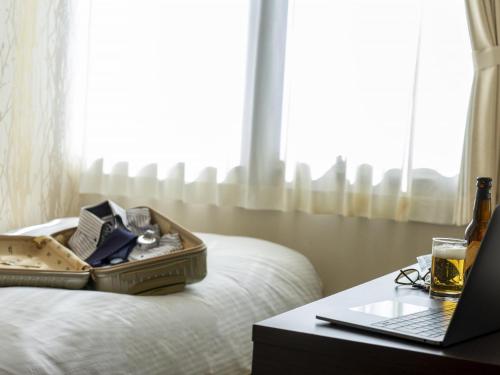 a suitcase on a bed next to a table with a laptop at Hotel New Gaea Domemae in Fukuoka