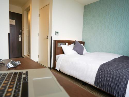 a bedroom with a bed and a desk with a keyboard at Hotel New Gaea Domemae in Fukuoka