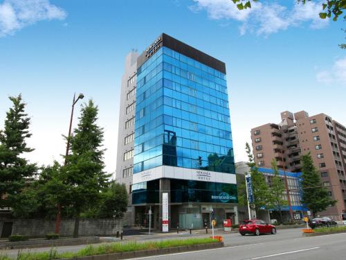 a tall glass building with a red car in front of it at Hotel New Gaea Domemae in Fukuoka