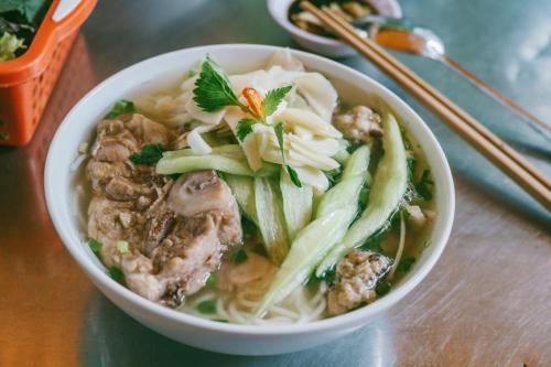 un tazón de sopa con carne y fideos en una mesa en Truong An NoiBai Airport Hotel en Noi Bai