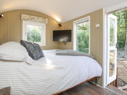 Sybs Farm Shepherds Hut في Fernhurst: غرفة نوم مع سرير أبيض كبير مع نوافذ