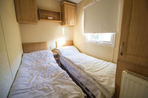 a small room with two beds and a window at Caravan With Decking At Manor Park In Hunstanton, Sleeps 6 Ref 23045b in Hunstanton
