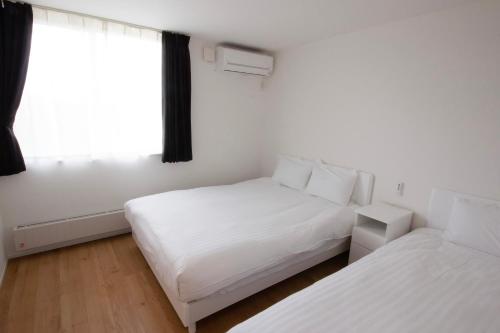 a white bedroom with two beds and a window at Yadoya YADOKARI 2nd in Pippu