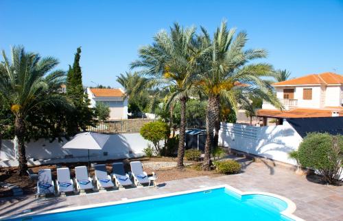 a swimming pool with chairs and palm trees at Villa Artemis in Larnaka