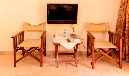 a room with two chairs and a table and a tv at Kalya Courts Hotel Fort Portal in Fort Portal