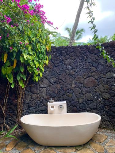 a bath tub sitting next to a stone wall with flowers at Villa Kepuh in Kubutambahan