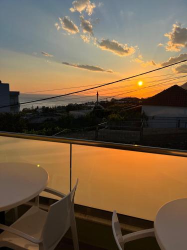 a sunset on a balcony with tables and chairs at Oscar’s Apartments Drymades in Dhërmi