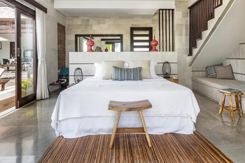 1 dormitorio con cama blanca grande y taburete de madera en Lumi Villa en Uluwatu