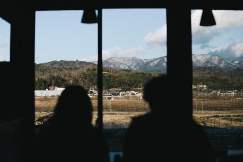 two people looking out of a window at mountains at 一棟貸しの古民家 燕と土と in Tokimata