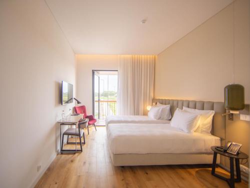 a hotel room with two beds and a desk and a window at Sines Sea View Business & Leisure Hotel in Sines