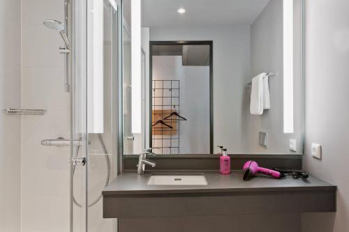 a bathroom with a sink and a shower with a mirror at Moxy Frankfurt City Center in Frankfurt/Main