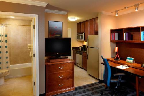 TownePlace Suites Houston North/Shenandoah في ذا وودلاندس: غرفة بها مكتب وتلفزيون ومطبخ