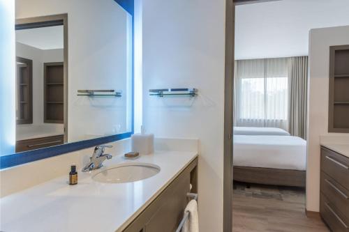 baño con lavabo, espejo y cama en Residence Inn by Marriott Playa del Carmen en Playa del Carmen