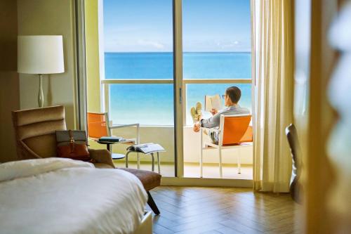 Ein Mann, der auf einem Stuhl sitzt und ein Buch vor einem Fenster liest. in der Unterkunft Marriott Stanton South Beach in Miami Beach