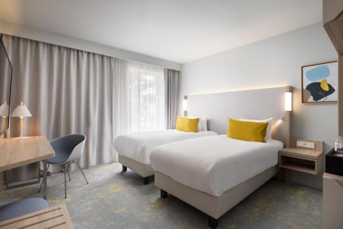 two beds in a hotel room with yellow pillows at Courtyard by Marriott Paris Charles de Gaulle Central Airport in Roissy-en-France