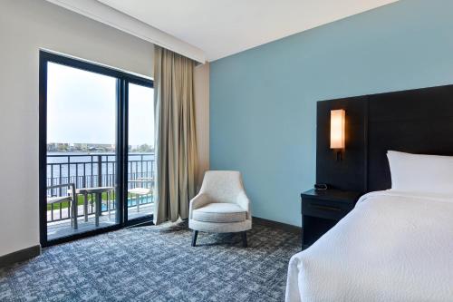 Residence Inn by Marriott Fort Walton Beach في شاطئ فورت والتون: غرفة نوم بسرير وكرسي وشرفة