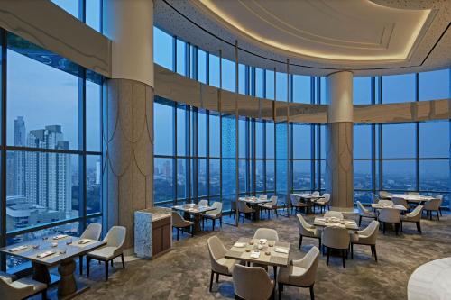 a restaurant with tables and chairs and large windows at The Westin Surabaya in Surabaya