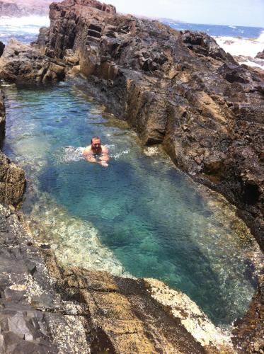 a man in a pool of water on a rocky beach at Villa Katerina in Caleta De Fuste