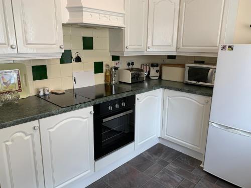 a white kitchen with white cabinets and black appliances at Acorn Cottage in Ollerton