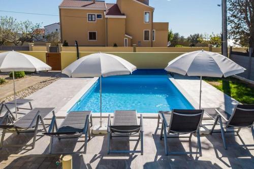 a group of chairs and umbrellas next to a pool at Villa Mattina, with heated pool and jacuzzi in Privlaka
