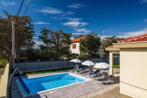 a swimming pool with chairs and umbrellas next to a house at Villa Mattina, with heated pool and jacuzzi in Privlaka
