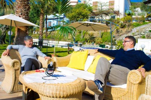 two men sitting in wicker chairs with a table and an umbrella at Hotel Piccolo Mondo in Acquappesa