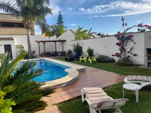 um quintal com uma piscina e cadeiras e uma casa em Villa Lolera em Chiclana de la Frontera
