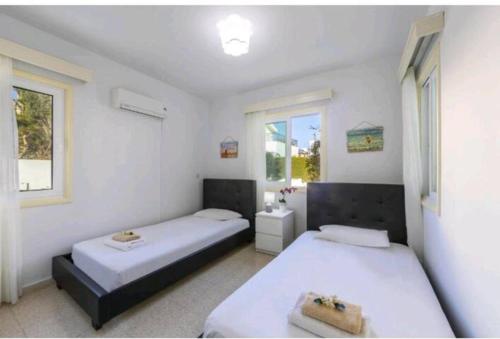 two beds in a room with white walls and windows at Protaras Fig Tree Bay Villa with Sea View &Jacuzzi in Protaras