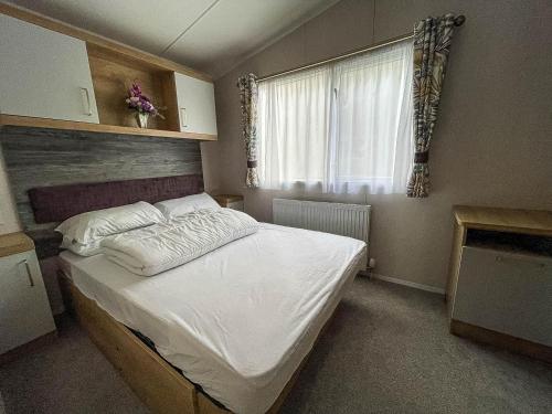 a bedroom with a large white bed with a window at Beautiful Caravan With Decking At Naze Marine Park, Sleeps 8 Ref 17341br in Walton-on-the-Naze