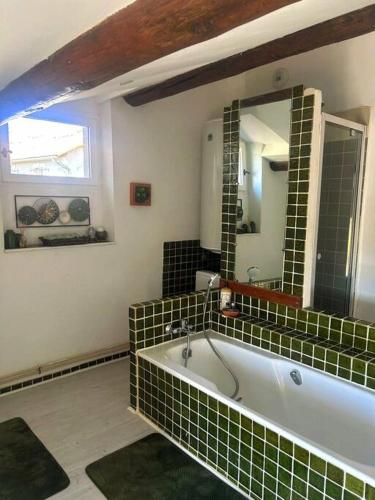 La salle de bains est pourvue d'une baignoire carrelée de vert et d'un miroir. dans l'établissement Au Micocoulier, à Châteauneuf-de-Gadagne
