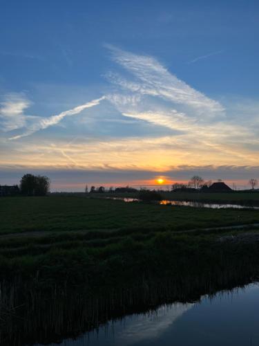 a sunset over a field with a river at Vakantiehuisjes Marsherne in Poppingawier