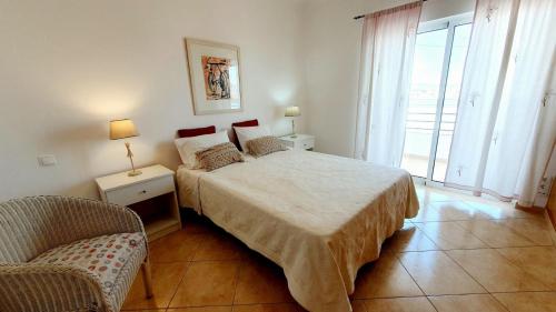 une chambre avec un lit, une chaise et une fenêtre dans l'établissement Quarteira Beach Vacation: 2BR steps to the sand, à Quarteira