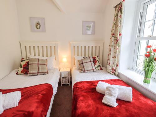 two beds in a small room with red sheets at The Old Post House at Low Stott Park in Ulverston