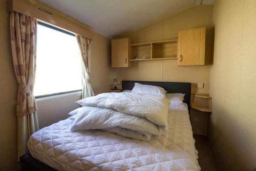 a bedroom with a bed with white sheets and a window at Lovely 6 Berth Caravan At Naze Marine Holiday Park In Essex Ref 17275c in Walton-on-the-Naze