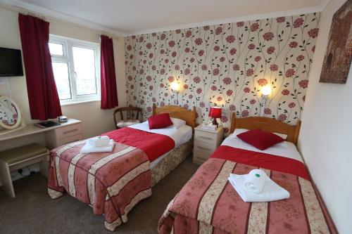 2 letti in camera d'albergo con tende rosse di Dorset Hotel, Isle of Wight a Ryde