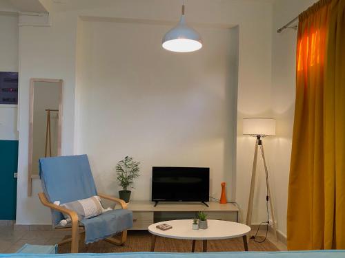 a living room with a blue chair and a tv at Helen's cozy studio (close to the airport) in Koropíon