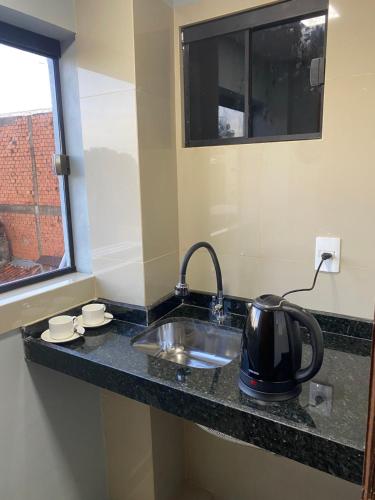 a kitchen counter with a sink and a tea kettle on it at España Suites Hotel in Ciudad del Este