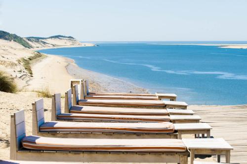 a row of wooden benches sitting on top of a beach at Hotel La Co(o)rniche in Pyla-sur-Mer