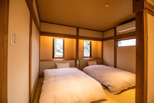 2 Betten in einem kleinen Zimmer mit 2 Fenstern in der Unterkunft Kyufukujyuin Takei Ryokan in Nagano