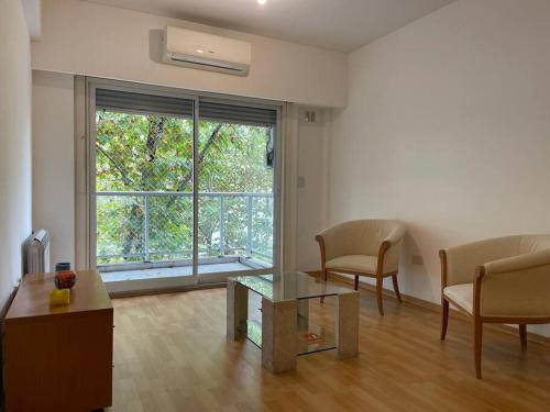 - un salon avec une table, des chaises et une grande fenêtre dans l'établissement Departamento 2 amb Villa Urquiza, à Buenos Aires
