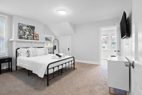 a white bedroom with a bed and a flat screen tv at Charming 3-Bedroom Home Near Downtown Free Parking in Pittsburgh