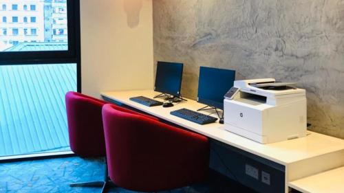 a desk with two computers and a printer and red chairs at Crowne Plaza - Dar Es Salaam by IHG in Dar es Salaam
