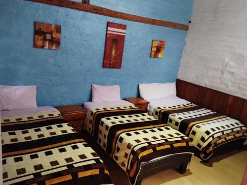 drie bedden in een kamer met blauwe muren bij Hostal La Catolica in Quito