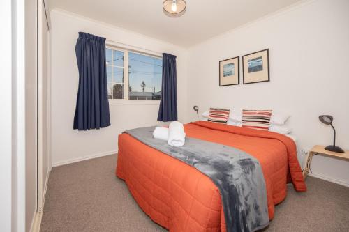 a bedroom with a bed with an orange blanket and a window at Relax on Rata, Cottage 1 in Twizel