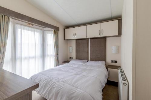 a bedroom with a large white bed with a window at Beautiful 6 Berth Caravan By The Beach In Suffolk Ref 40076nd in Lowestoft