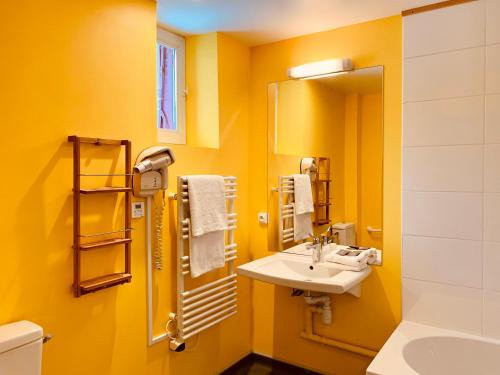 Baño amarillo con lavabo y espejo en Hotel Restaurant Le Clos, en Besse-et-Saint-Anastaise