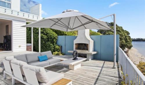 eine Terrasse mit einem Sonnenschirm, einer Couch und einem Kamin in der Unterkunft Once Upon a Tide in Auckland