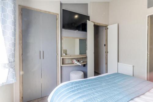 a bedroom with a blue bed and a closet at Stunning 6 Berth Lodge With Partial Sea Views In Suffolk Ref 68007cr in Lowestoft
