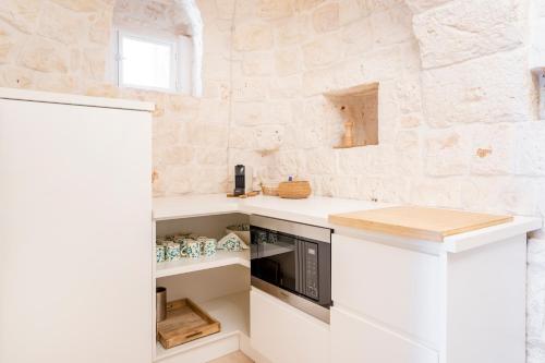 a kitchen with white cabinets and a stone wall at Trulli Cicerali , trulli design con piscina panoramica in Ostuni