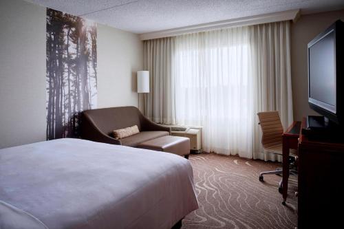 a hotel room with a bed and a chair and a television at Detroit Metro Airport Marriott in Romulus